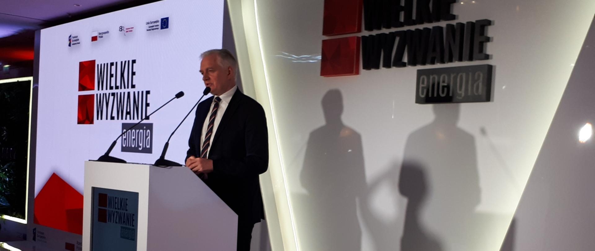 Minister Gowin mówi do mikrofonu. Stoi na tle ściany z napisem wielkie wyzwanie.