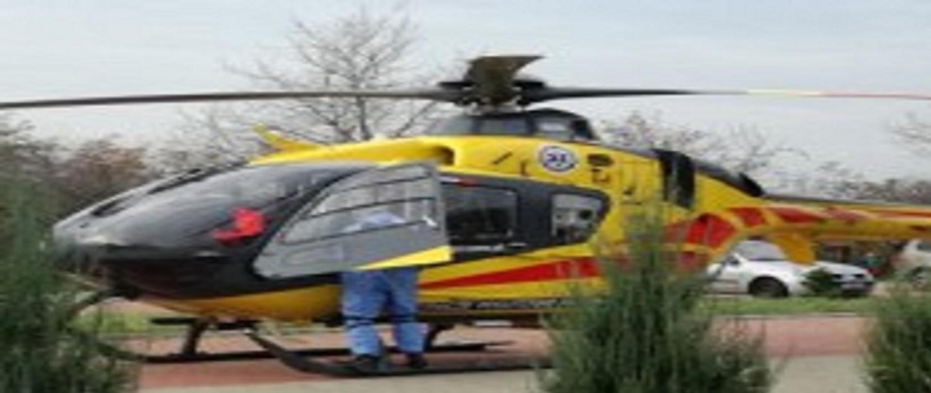 Zdjęcie przedstawia stojący śmigłowiec Lotniczego Pogotowia Ratunkowego. Przy otwartych drzwiach stoi pilot. 