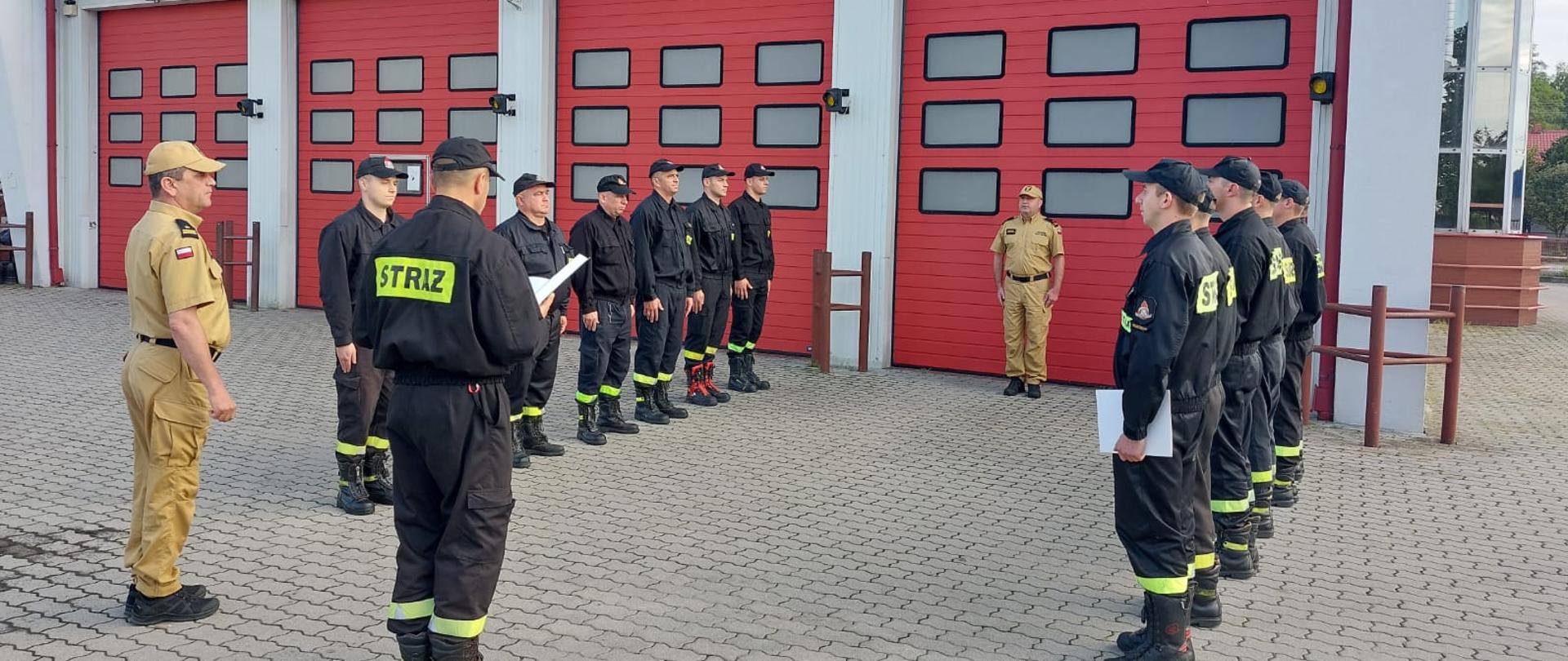 Plac wewnętrzny KP PSP we Włoszczowie, przed garażami ustawione dwie zmiany służbowe, dowódca zmiany przyjmującej odczytuje rozkaz.