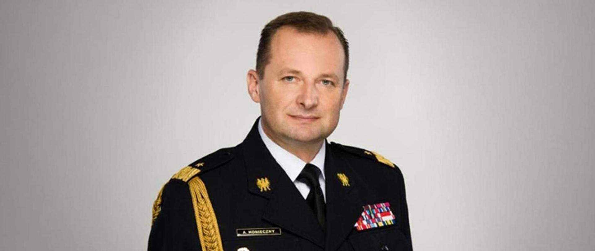 Zdjęcie przedstawia Zastępce Komendanta Głównego Państwowej Straży Pożarnej w mundurze galowym na szarym tle