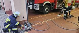 Sprawianie urządzeń hydraulicznych przez strażaków. W tle samochód pożarniczy