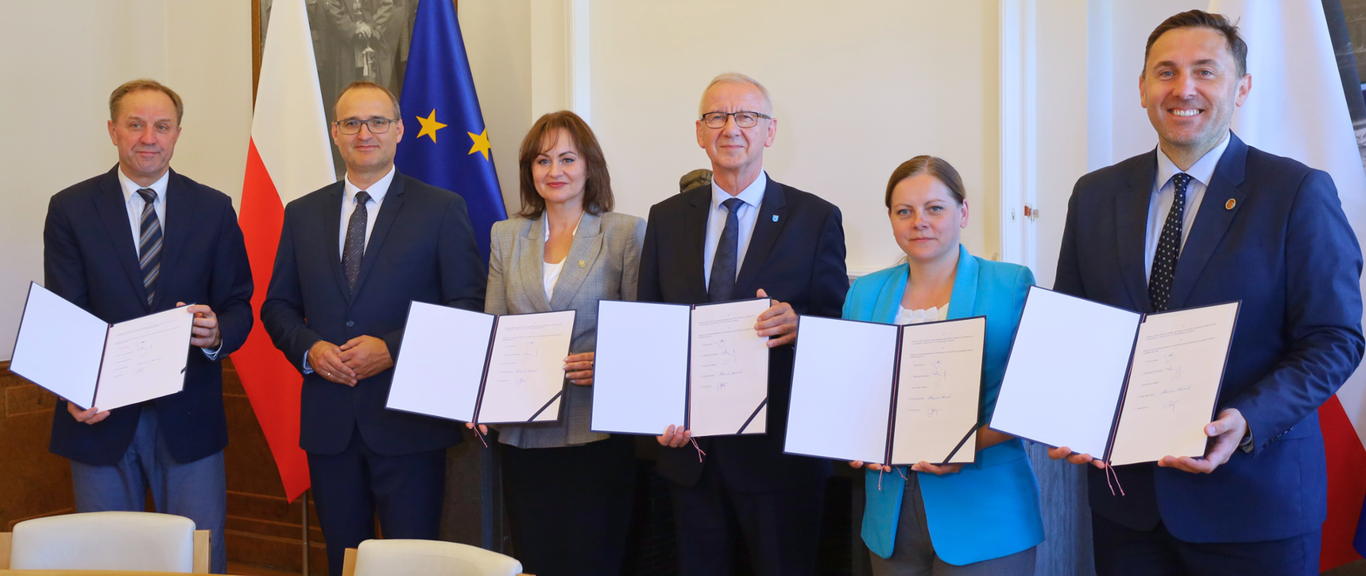 kilka osób - kobiety i mężczyźni stoją i prezentują podpisane wcześniej umowy