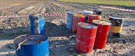 Dziesięć beczek 200 litrowych w kolorach niebieskim (trzy), czerwonym (cztery) i czarnym (trzy) stoi na ziemi na otwartym, płaskim terenie.