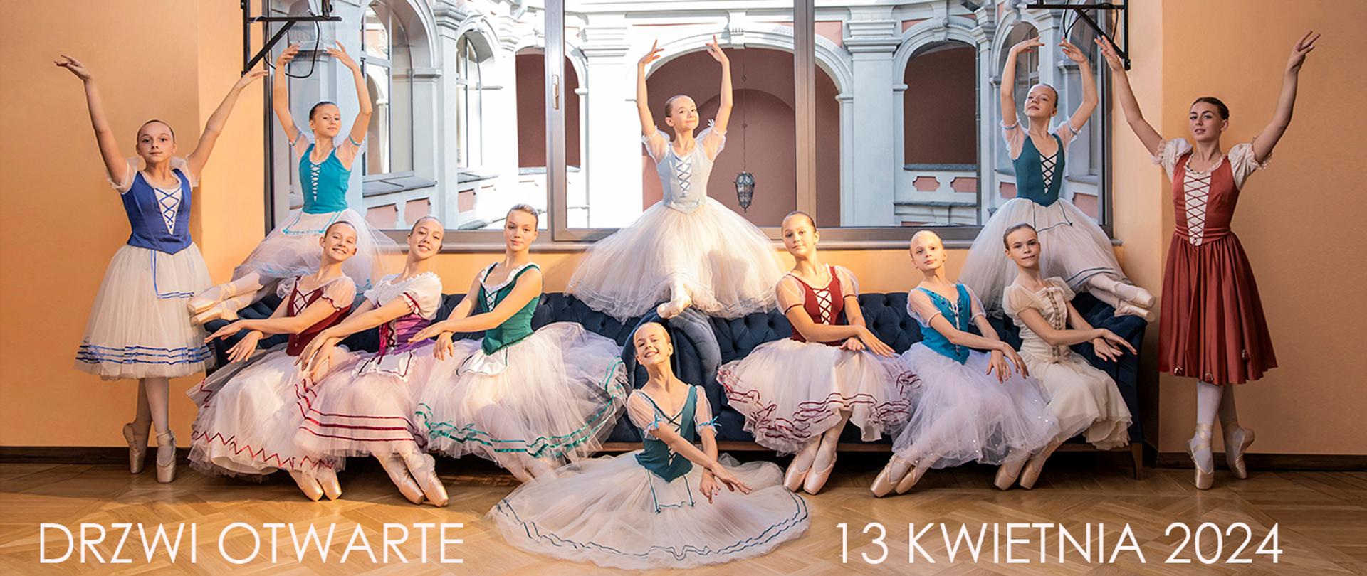 Tancerki w kolorowych strojach, część siedząca na długiej sofie pod wielkim przeszklonym oknem, część stoi, jedna tancerka siedzi na podłodze przed wszystkimi pozostałymi