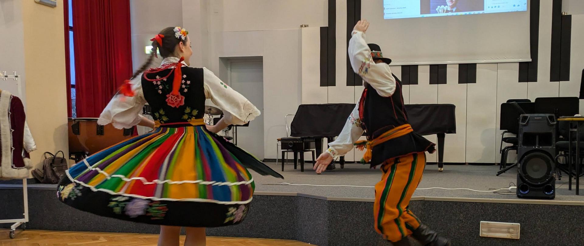 Kobieta i mężczyzna w strojach łowickich tańczą.