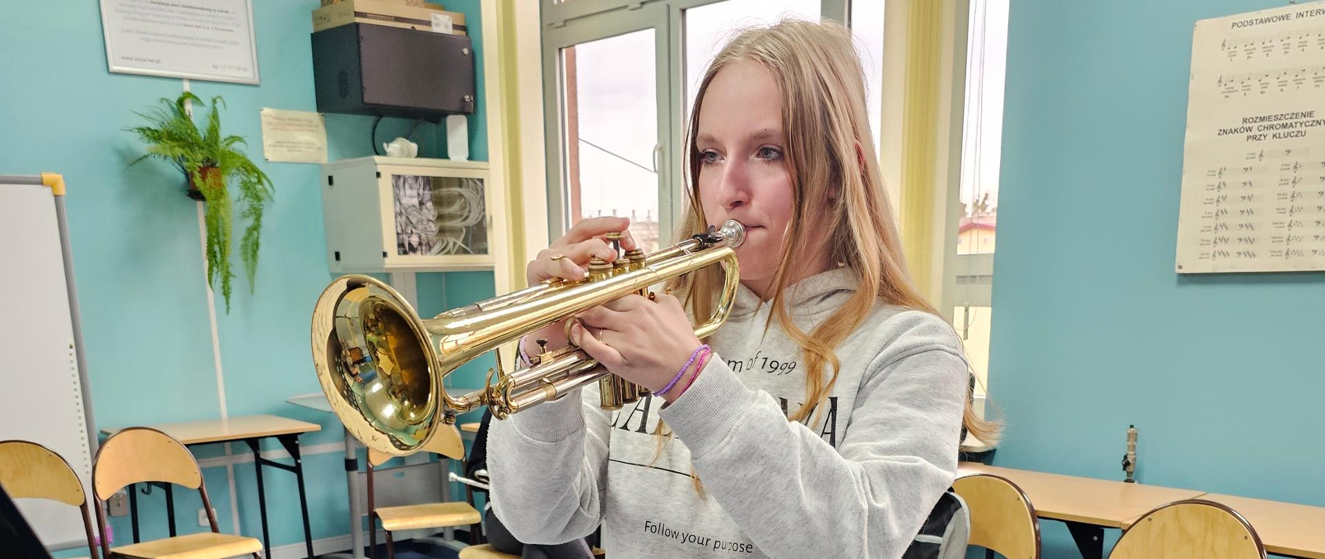 Warsztaty trąbkowe. Uczeń gra na trąbce. Inni uczniowie słuchają. Sala lekcyjna. Pulpit.