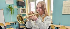 Warsztaty trąbkowe. Uczeń gra na trąbce. Inni uczniowie słuchają. Sala lekcyjna. Pulpit.