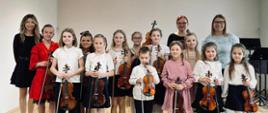 Grupa uczniów stoi na scenie sali koncertowej, w rękach trzymają skrzypce