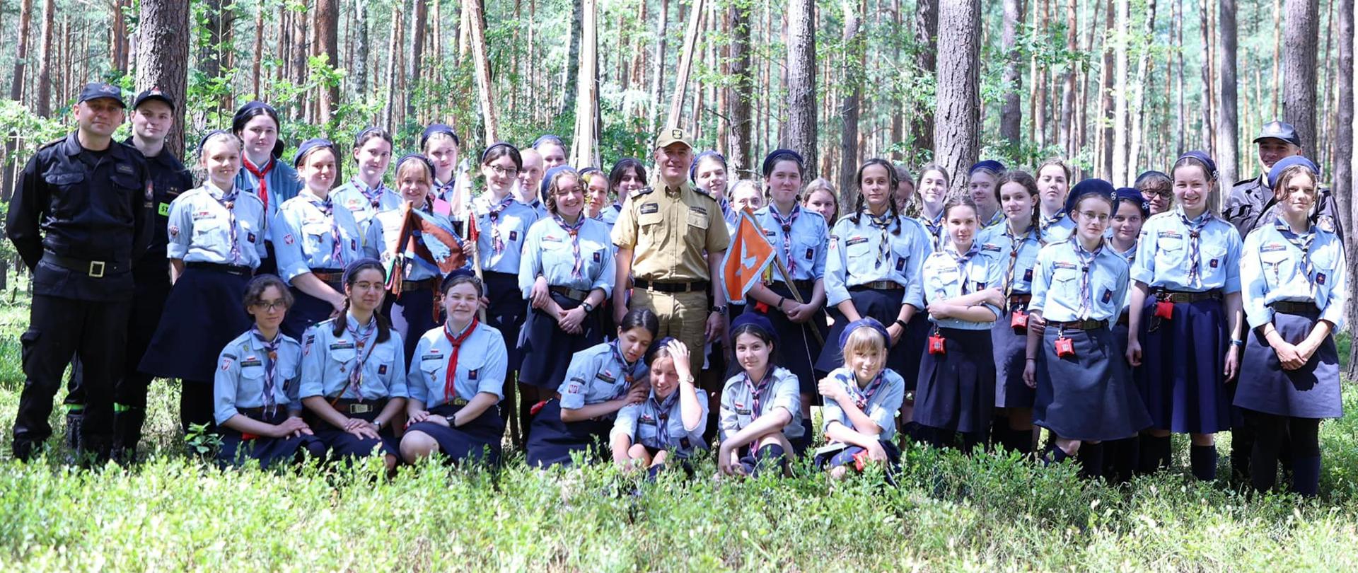 Na zdjęciu widać komendanta głównego PSP, strażaków z KP PSP Ostrów Mazowiecka oraz 14 Warszawski Szczep Skautów Europy. W tle las.