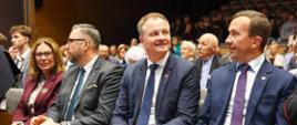 grupa oficjeli w tym wicewojewoda, siedzą na widowni, rozmawiają ze sobą 