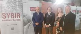A group of four people pose for a photo; from left, Chargé d'Affaires Jacek Chodorowicz, Director of the Sybir Memorial Museum, Prof. Wojciech Śleszyński, Julita Waś, and President of the Polish Association of Siberian Deportees of South Africa, Stefan Szewczuk; posters from the "Sybir: Prison of Nations" exhibition in the background.