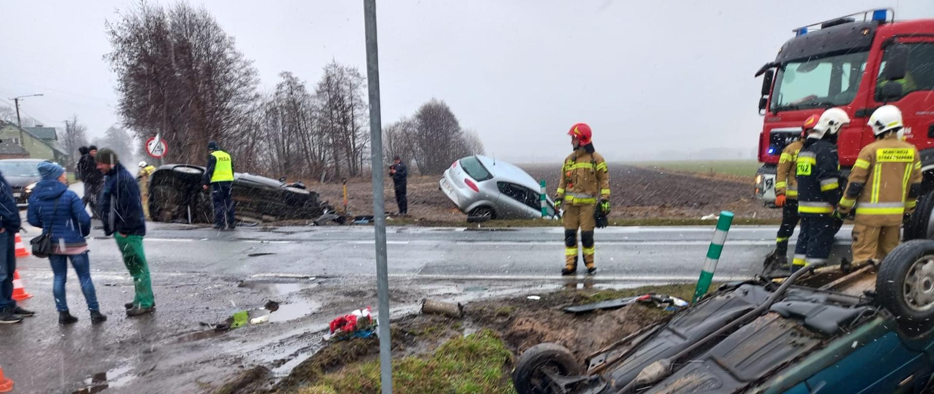 Samochody po wypadku znajdują się rowie. Na drodze samochód strażacki.