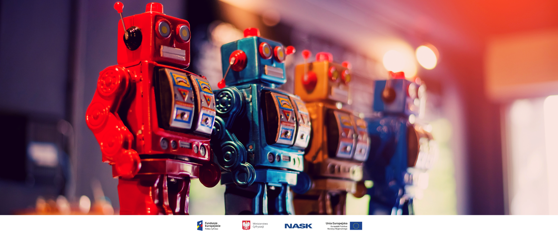 Na zdjęciu widać cztery stojące obok siebie zabawkowe roboty - im dalej w prawo tym obraz jest bardziej rozmyty, tak że ostatni z robotów jest mało wyraźny i niknie w odblaskach świetlnych. U dołu znajduje się pasek logotypów: Europejskie Fundusze Polska Cyfrowa, Ministerstwo Cyfryzacji, NASK i Unia Europejska Europejski Fundusz Rozwoju Regionalnego.