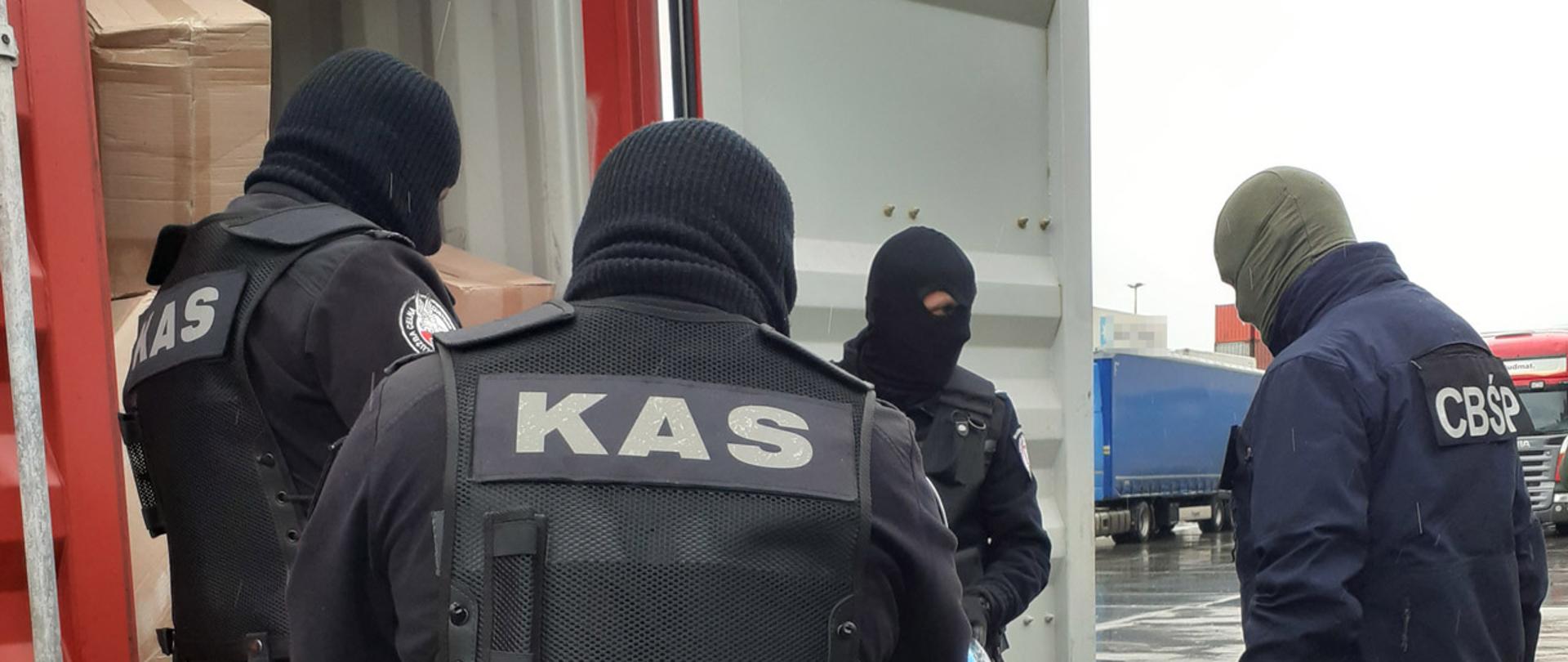 Czterech funkcjonariuszy KAS i CBŚP przy otwartym kontenerze z papierosami.
