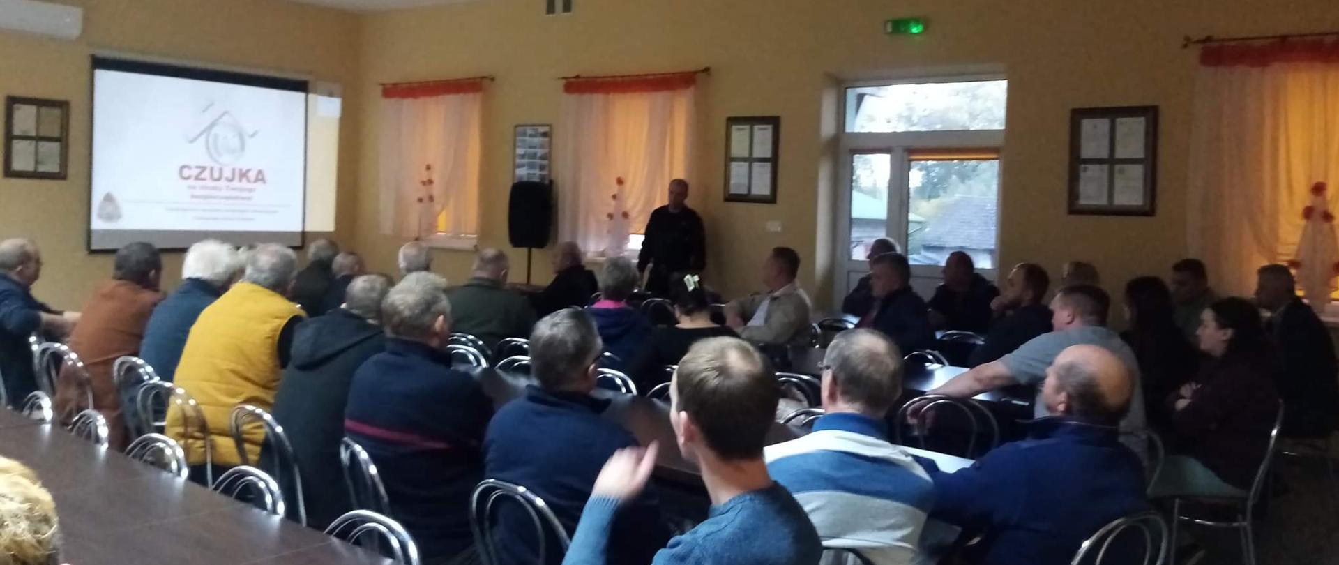 Spotkanie z mieszkańcami. Funkcjonariusz KP PSP w Oleśnie omawia zagadnienia związane z czujkami tlenku węgla.