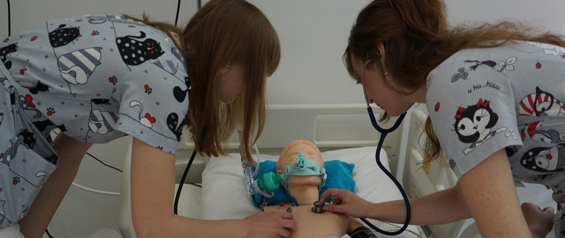 Studentki nachylone nad łóżkiem, na którym leży fantom do ćwiczeń