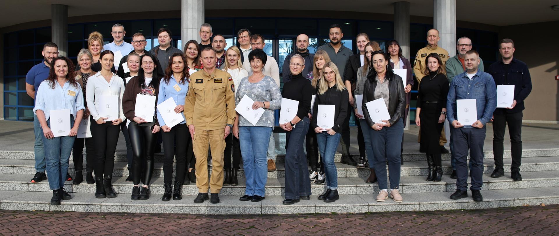 Pamiątkowe zdjęcie grupowe uczestniczek i uczestników szkolenia inspektorów ochrony przeciwpożarowej (30 osób) w towarzystwie Zastępcy Komendanta Centralnej Szkoły PSP oraz kobiety i funkcjonariusza CS PSP