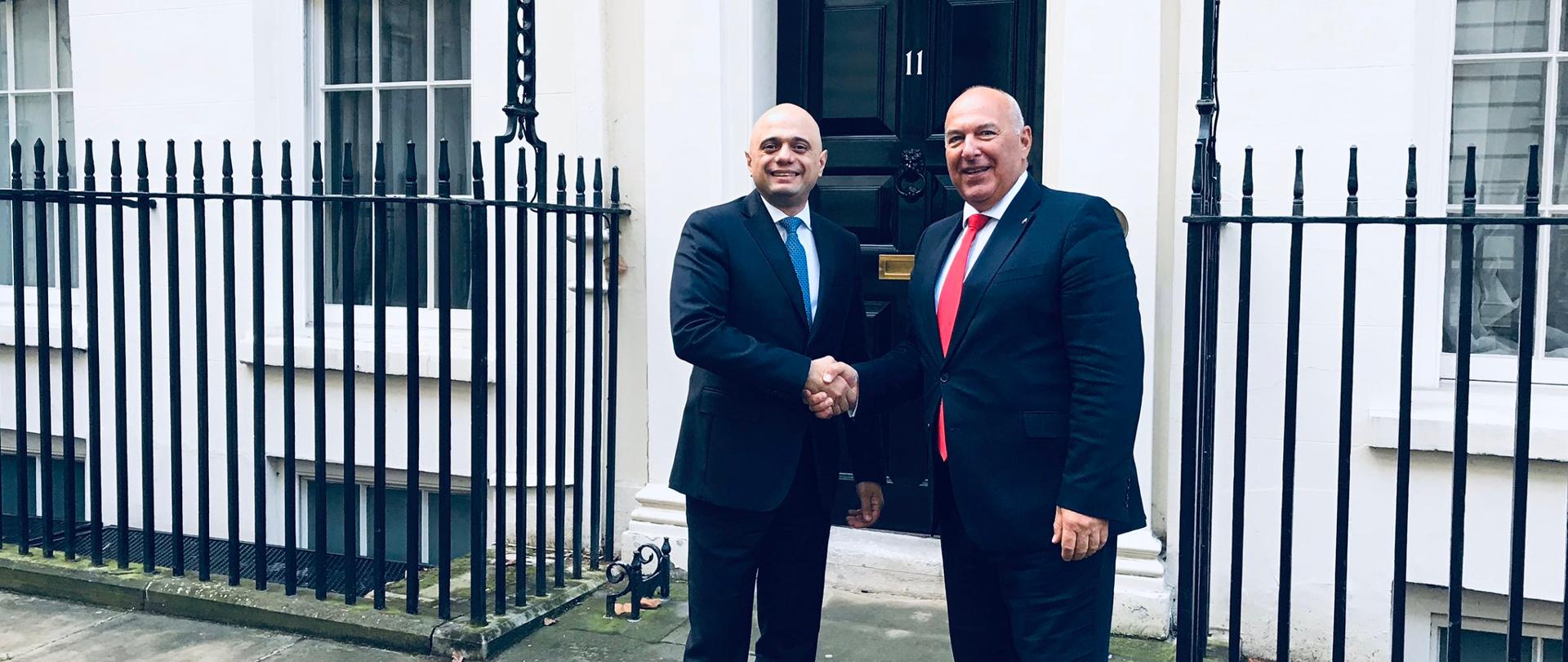 Uśmiechnięty minister Tadeusz Kościński i brytyjski kanclerz skarbu Sajidem Javidem witają się podając sobie ręce. 