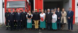 zdjęcie przed remizą strażacką na tle garaże z samochodem strażackim na pierwszym planie Mazowiecki Komendant Wojewódzki, zaproszeni gości, druhowie OSP i koło gospodyń wiejskich