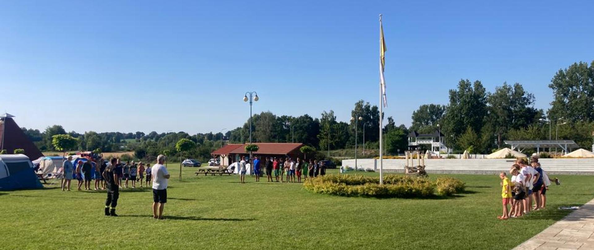 Na zdjęciu strażak przed grupą dzieci biorących udział w turnusie obozowym
