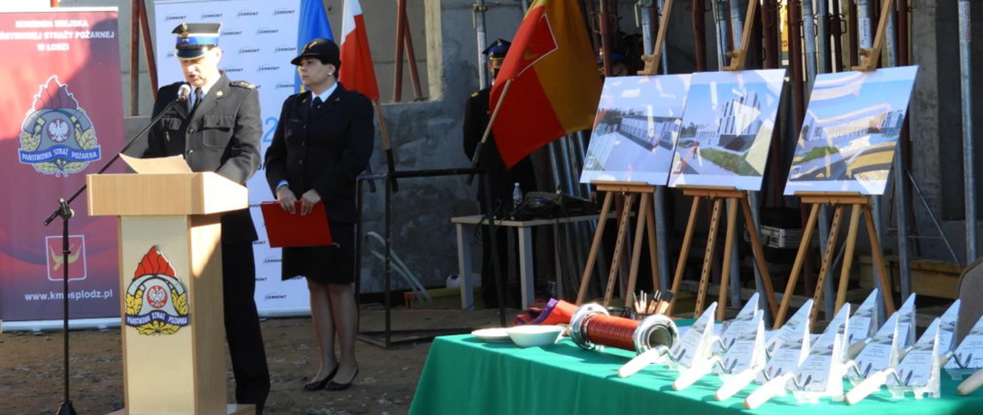 Na zdjęciu widać funkcjonariuszy PSP prowadzących uroczystość, stół z ozdobnymi kielniami przygotowanymi do wmurowania aktu erekcyjnego oraz obrazy z wizualizacją nowej jednostki ratowniczo-gaśniczej