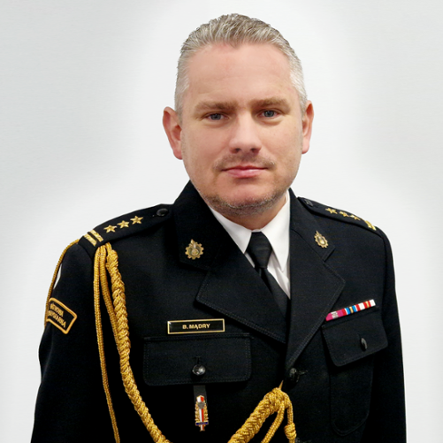 Zdjęcie przedstawia st. bryg. Bartłomieja Mądrego Zastępcę Lubuskiego Komendanta Wojewódzkiego PSP w Gorzowie Wlkp. w mundurze na szarym tle. 