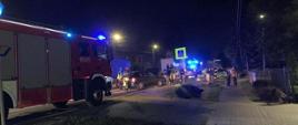 Strażacy pracujący przy zdarzeniu na drodze, w tle pojazd pożarniczy, pora nocna