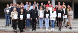 Grupowe zdjęcie uczestników szkolenia (26 osób) w towarzystwie Zastępcy Komendanta Centralnej Szkoły PSP, kobiety oraz dwóch funkcjonariuszy CS PSP