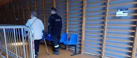na zdjęciu z prawej strony strażak pomagający osobie potrzebującej dotrzeć na miejsce w punkcie szczepień.