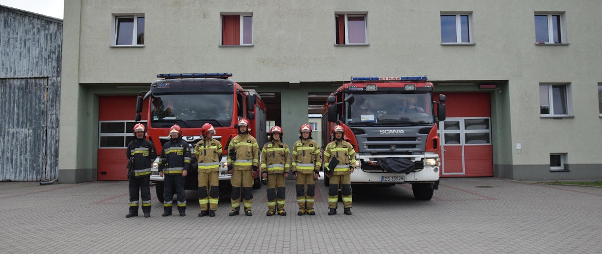 Strażacy z KP PSP Szczecinek oddali Hołd Powstańcom w kolejną rocznicę wybuchu Powstania Warszawskiego. Strażacy ubrani w ubrania specjalne, stoją na tle samochodów pożarniczych.