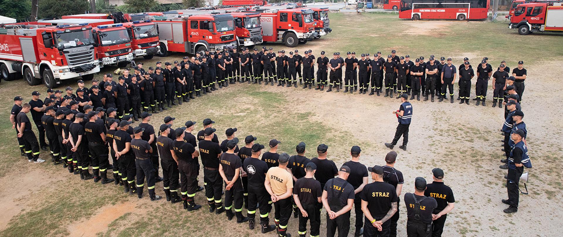 Funkcjonariusze Państwowej Straży Pożarnej na wyspie Evia. W tle stoją wozy strażackie.