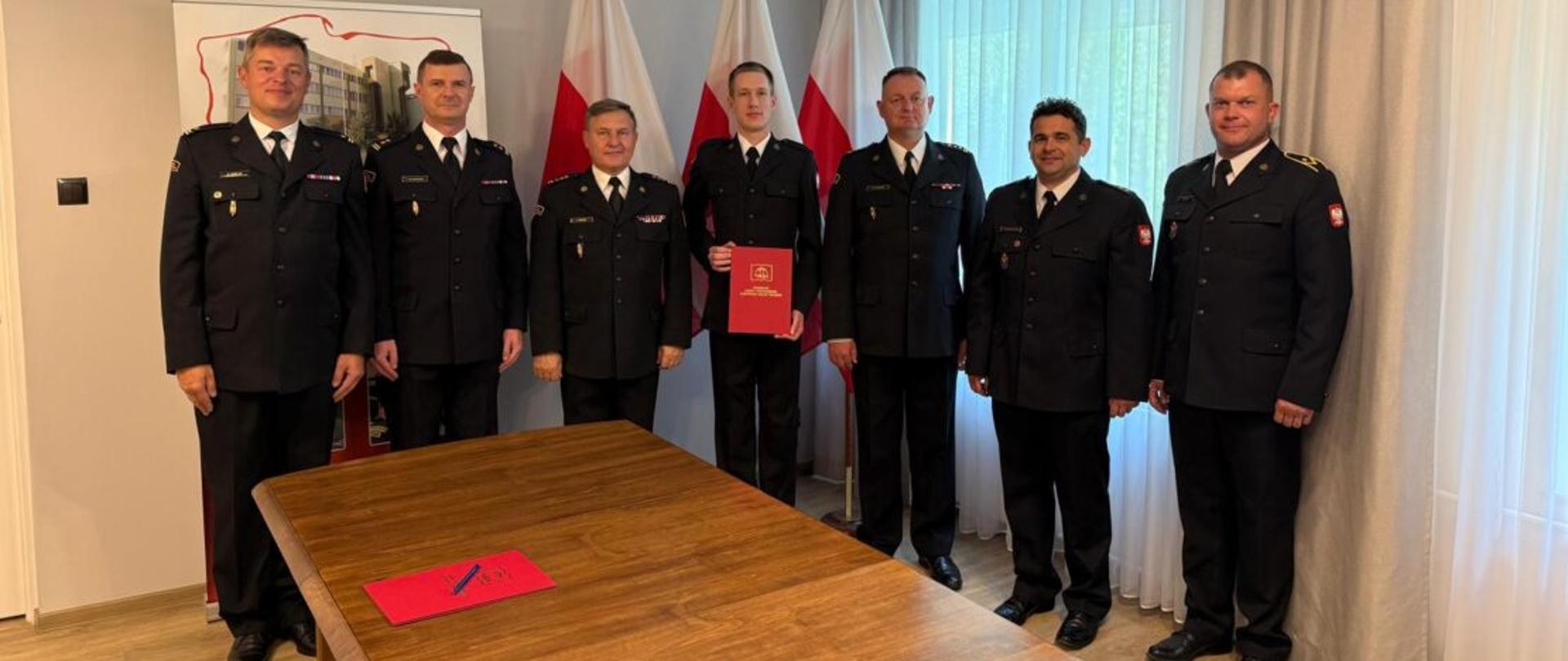 Na zdjęciu widać strażaków w mundurach galowych, w tle Polskie flagi i godło