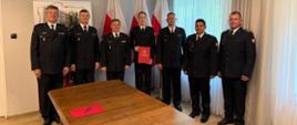Na zdjęciu widać strażaków w mundurach galowych, w tle Polskie flagi i godło