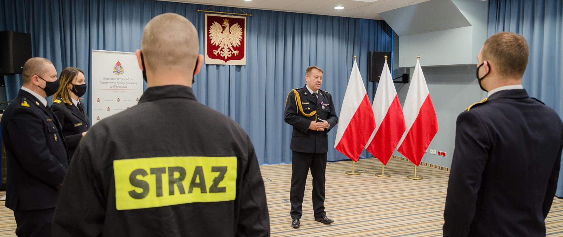 Na zdjęciu pięciu strażaków w tle trzy flagi Polski oraz godło RP