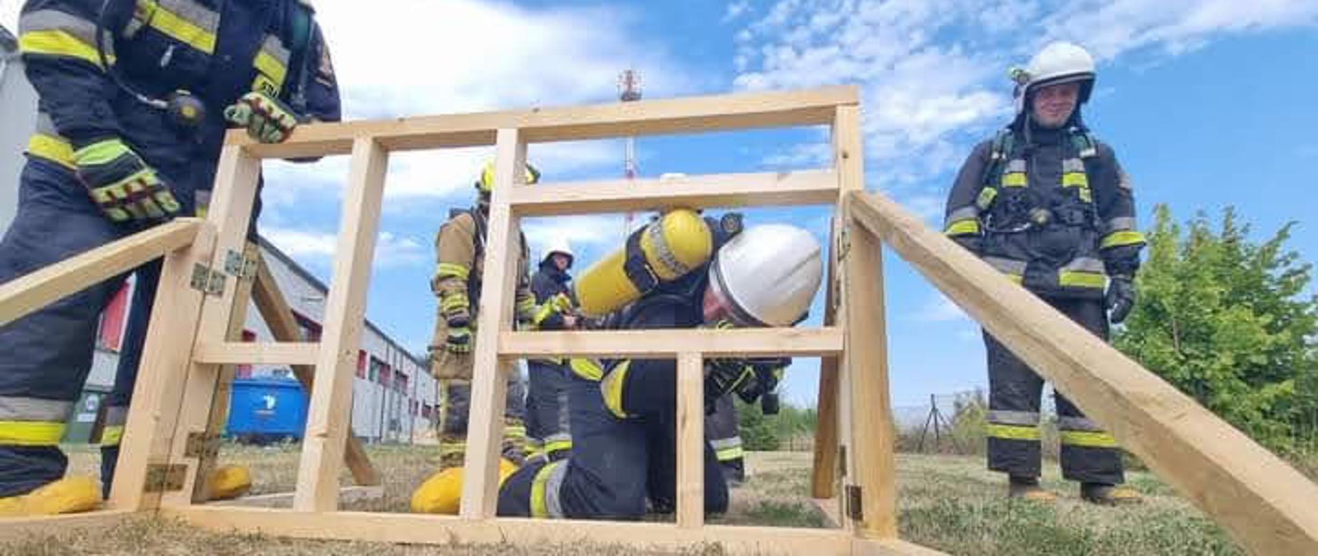 Na zdjęciu znajdują się druhowie podczas ćwiczeń praktycznych ze sprzętu ochrony układu oddechowego. Zdjęcie wykonano podczas pokonywania przeszkody przez jednego z druhów. 
