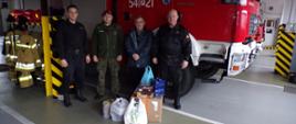 Zdjęcie przedstawia symboliczne przekazanie organizatorom akcji Murem za polskim Mundurem na terenie powiatu ostrzeszowskiego artykułów spożywczych dla funkcjonariuszy pełniących służbę na granicy wschodniej. Na zdjęciu widzimy funkcjonariuszy Komendy PSP wraz z organizatorami zbiórki. Zdjęcie wykonane w porze dziennej na garażu JRG
