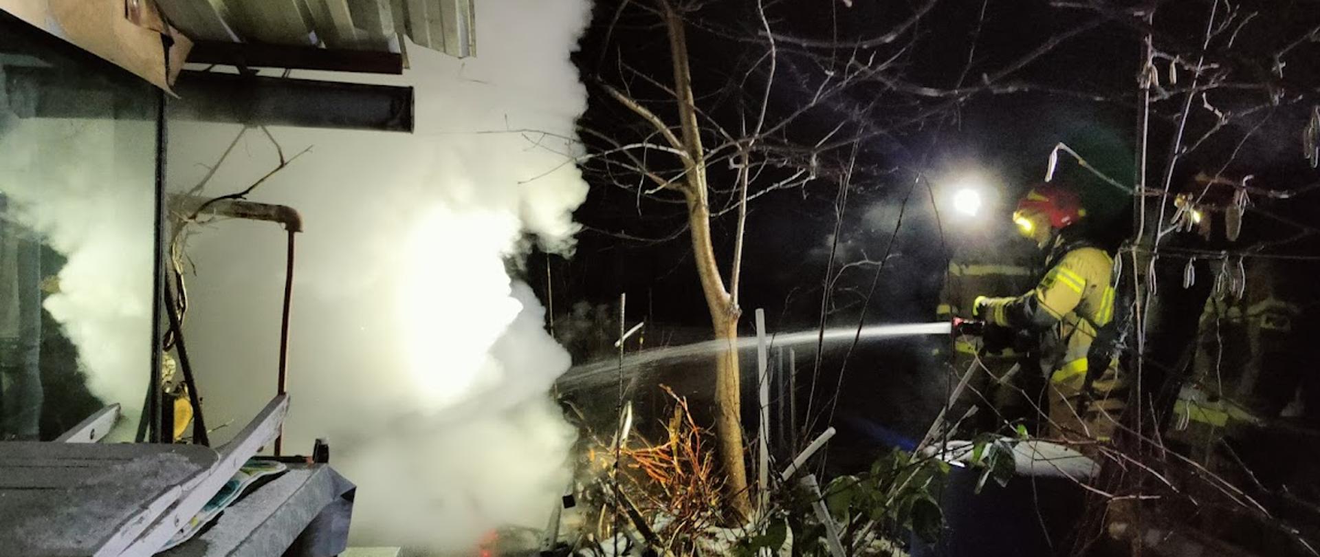 Strażak prowadzi działania gaśnicze. Przed nim obłok dymu i pary wodnej.