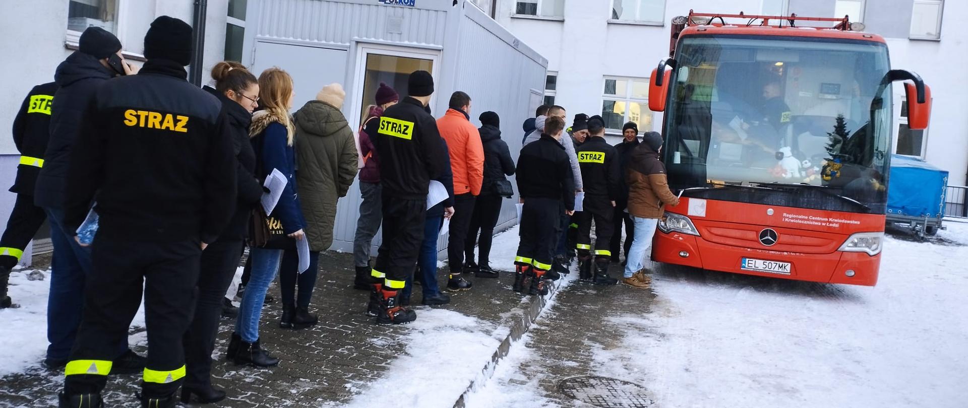Przed autobusem do oddania krwi stoi kolejka ludzi wśród nich strażacy