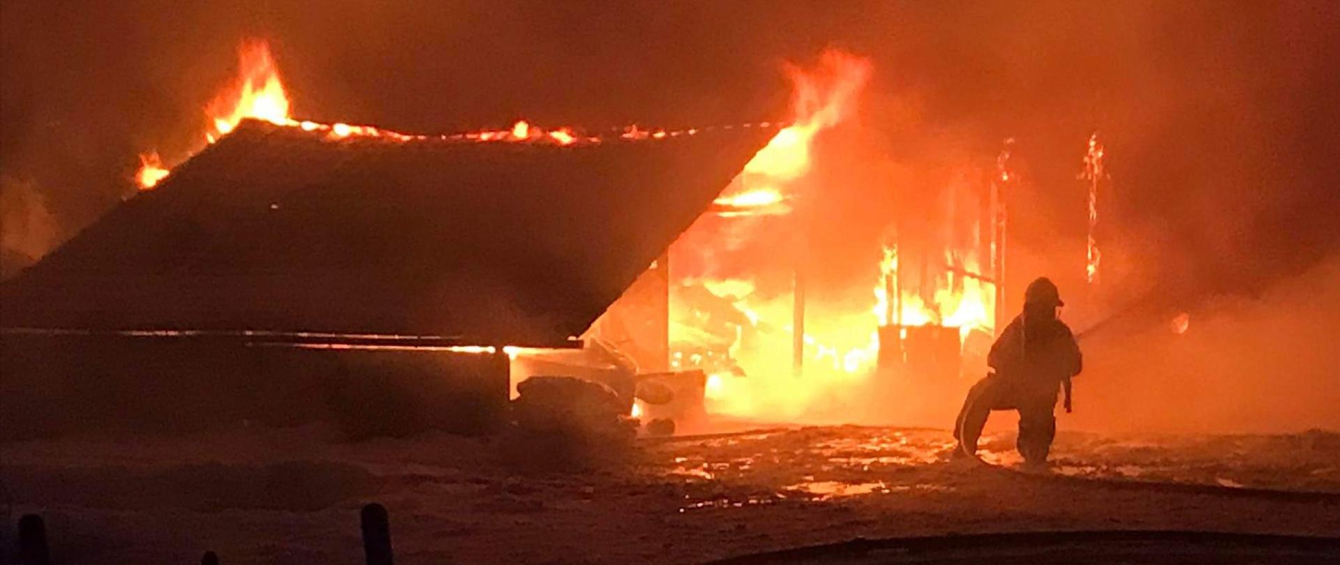 Zdjęcie przedstawia strażaka gaszącego pożar budynku.