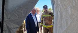 Strażak omawia mężczyźnie działanie namiotu do dekontaminacji za nimi stoi mężczyzna.