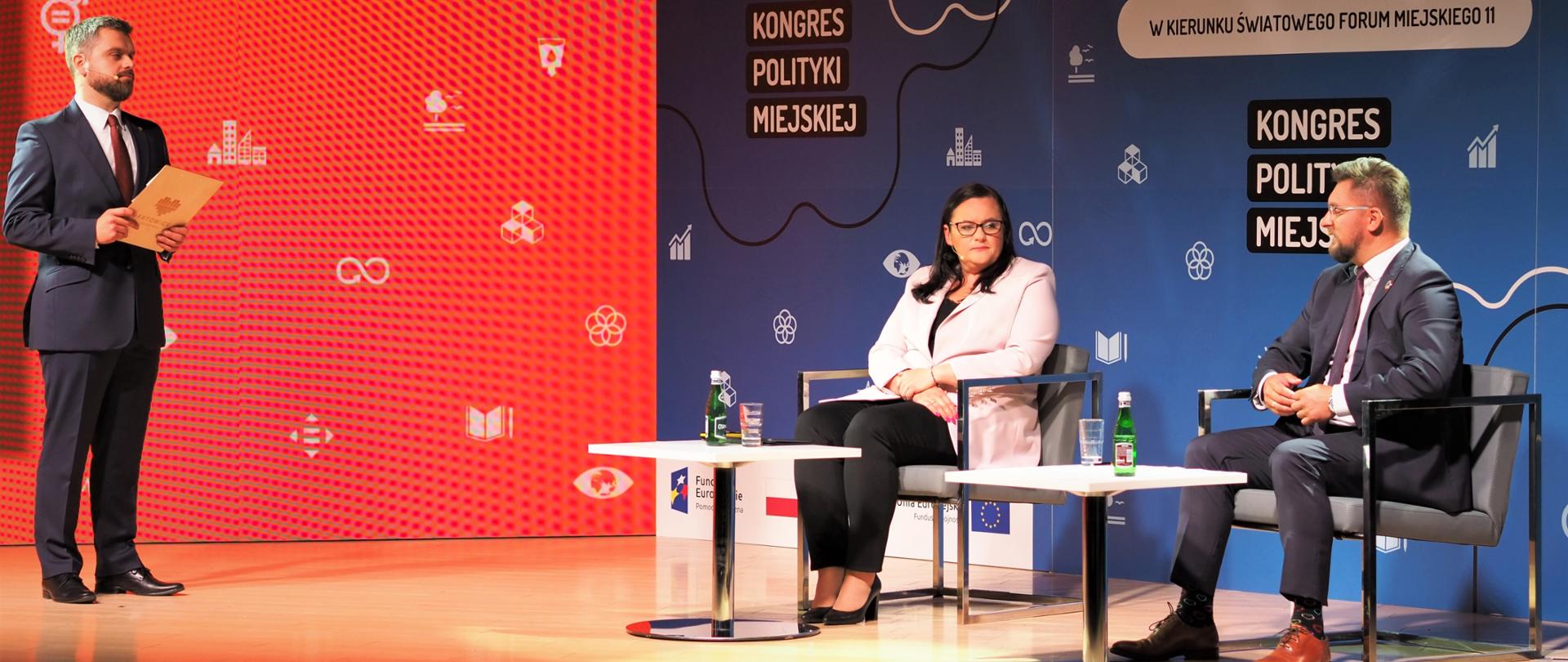 na scenie stoi prowadzący transmisję, przy stolikach siedzą wiceminister Małgorzata Jarosińska-Jedynak i prezydent Katowic Marcin Krupa