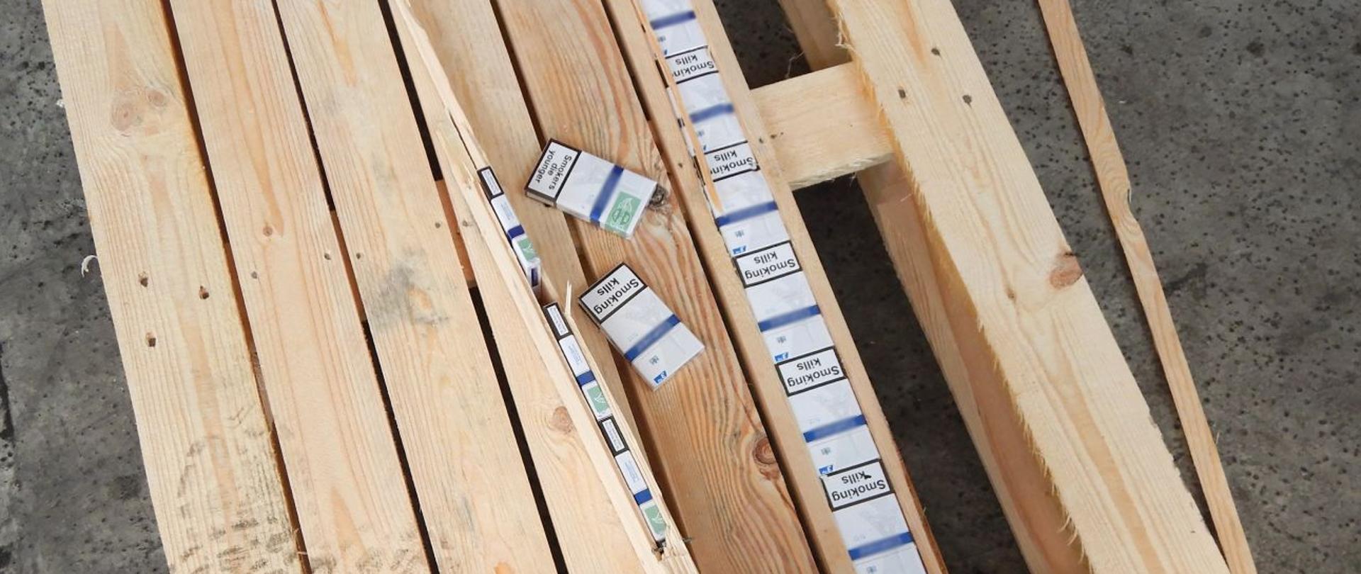 Rozbita paleta, widoczne paczki z papierosami ukryte w deskach.