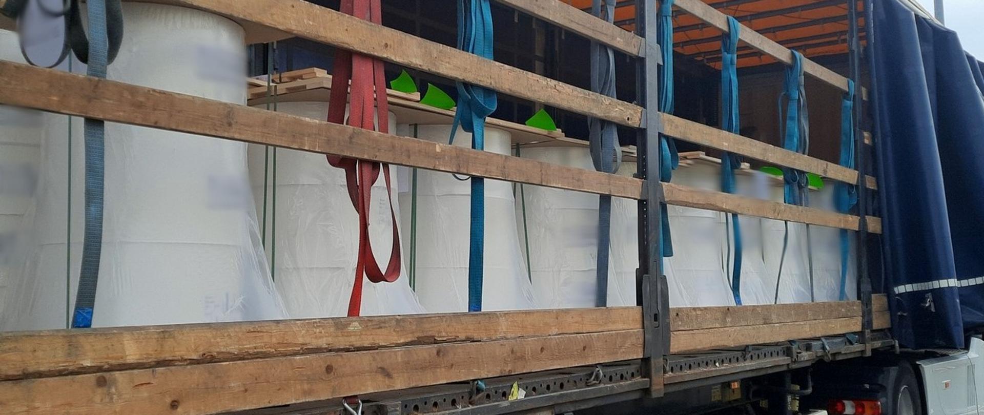 Naczepa ciężarowa z odsuniętą plandeką. Ładunek w postaci 11 ton bel papieru ustawionych na paletach nie jest spięty ani jednym pasem mocującym lub przegrodzony belką poprzeczną. Na deskach nad burtami wiszą pasy transportowe.