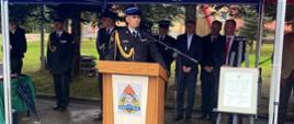 Na zdjęciu widoczny Komendant Powiatowy PSP w Gorlicach przemawiający przy mównicy a za nim w tle goście uczestniczący w uroczystość włączenia OSP Rożnowice do KSRG