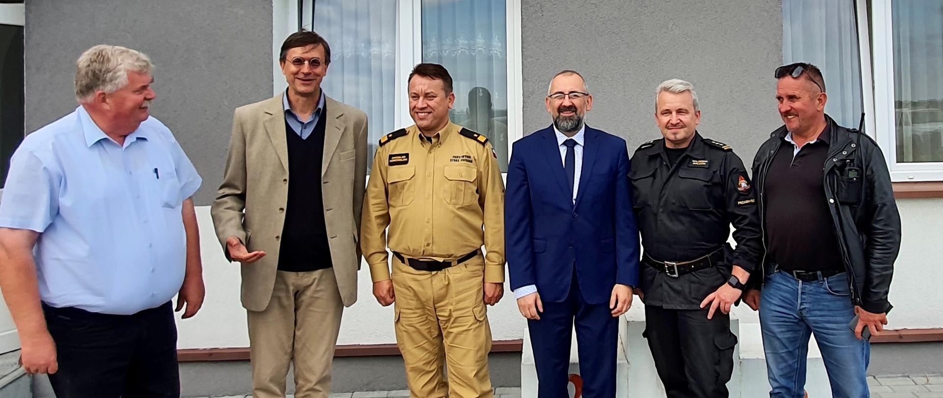 Na zdjęciu widać sześć osób. W tle ściana budynku w kolorze szarym, u góry napis na budynku Lotnisko Przasnysz, Politechnika Warszawska.