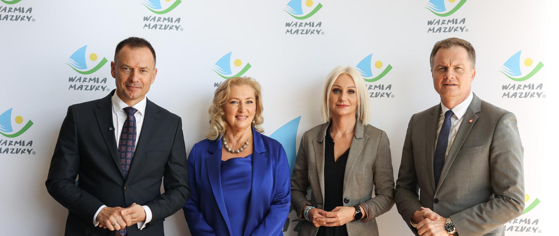 przedstawiciele branży turystycznej na tle białej ścianki z logiem województwa warmińsko-mazurskiego