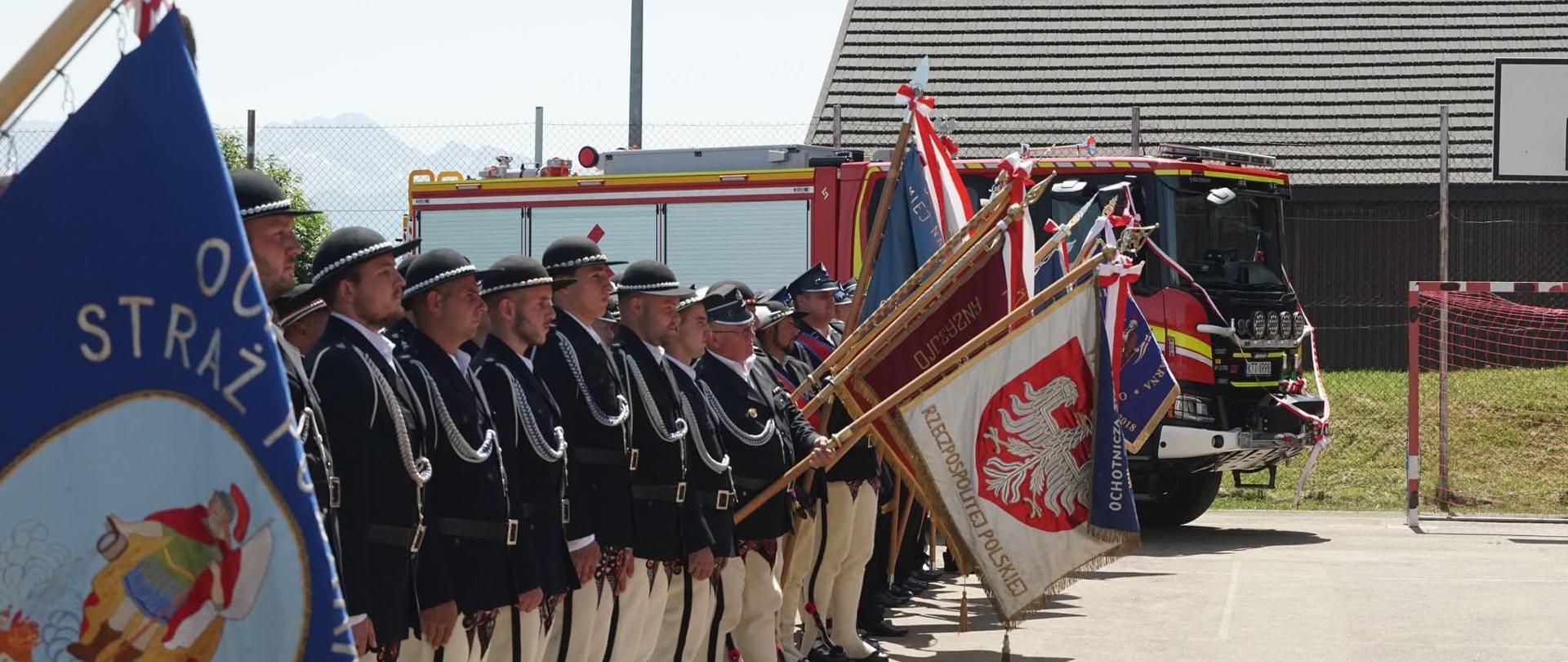 Strażacy pochylający sztandar ubrani po góralsku