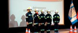 Zdjęcie przedstawia druhów MDP podczas pokazu udzielania pierwszej pomocy. Druhowie stoją na scenie ubrani w stroje strażackie. 