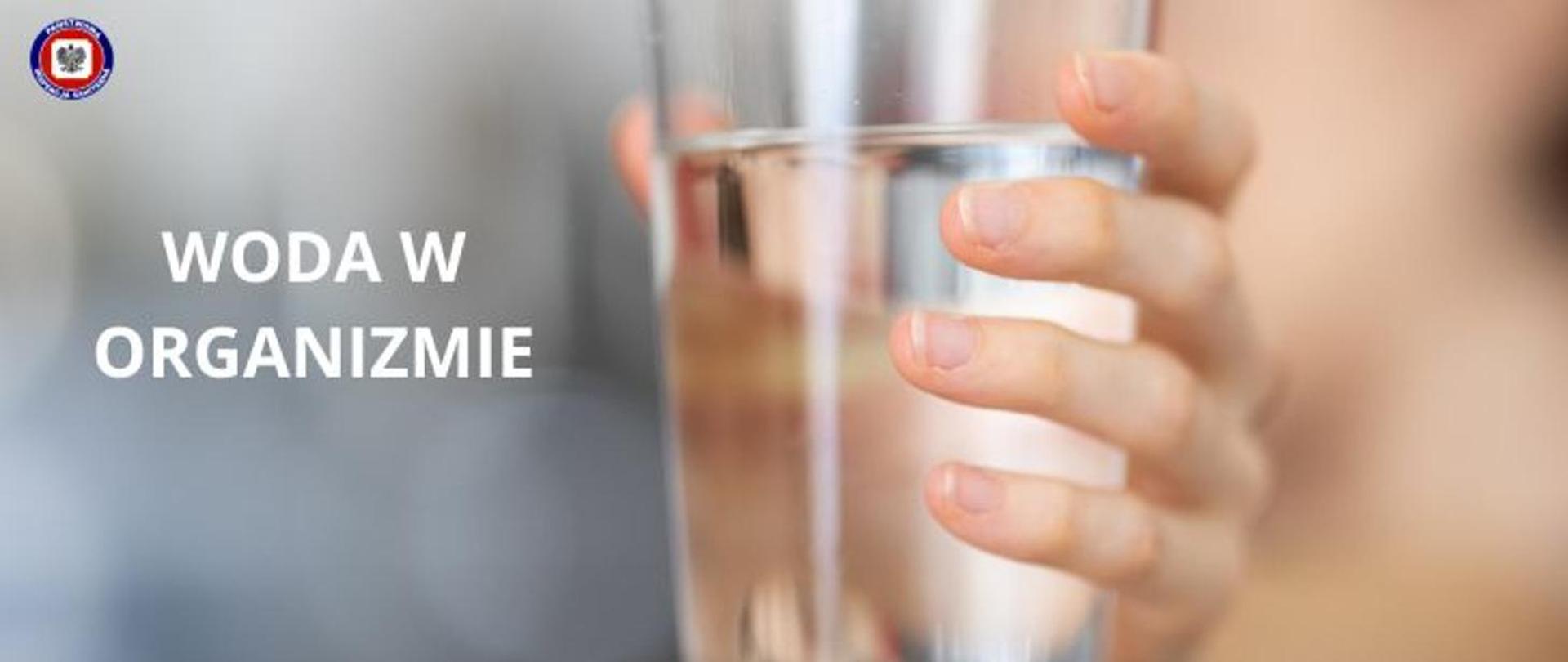 Na grafice widzimy dłoń trzymającą szklankę z wodą.