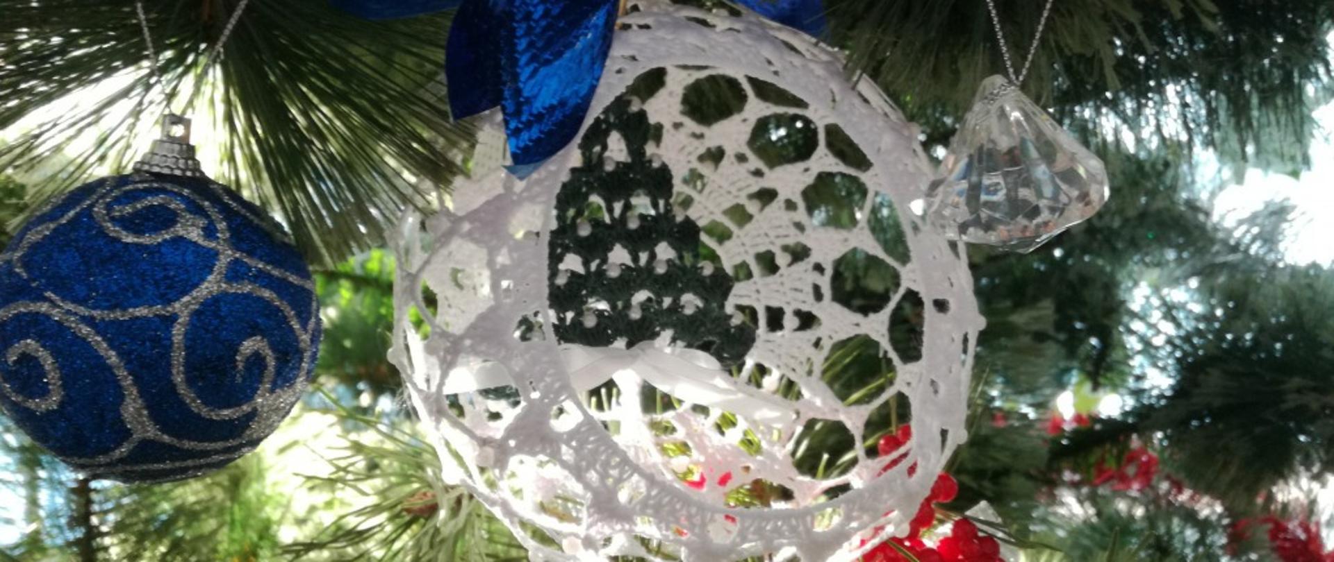 Na zdjęciu w centralnym jego miejscu znajdują się bombki choinkowe po lewej niebieska po prawej biała zawieszone na choince